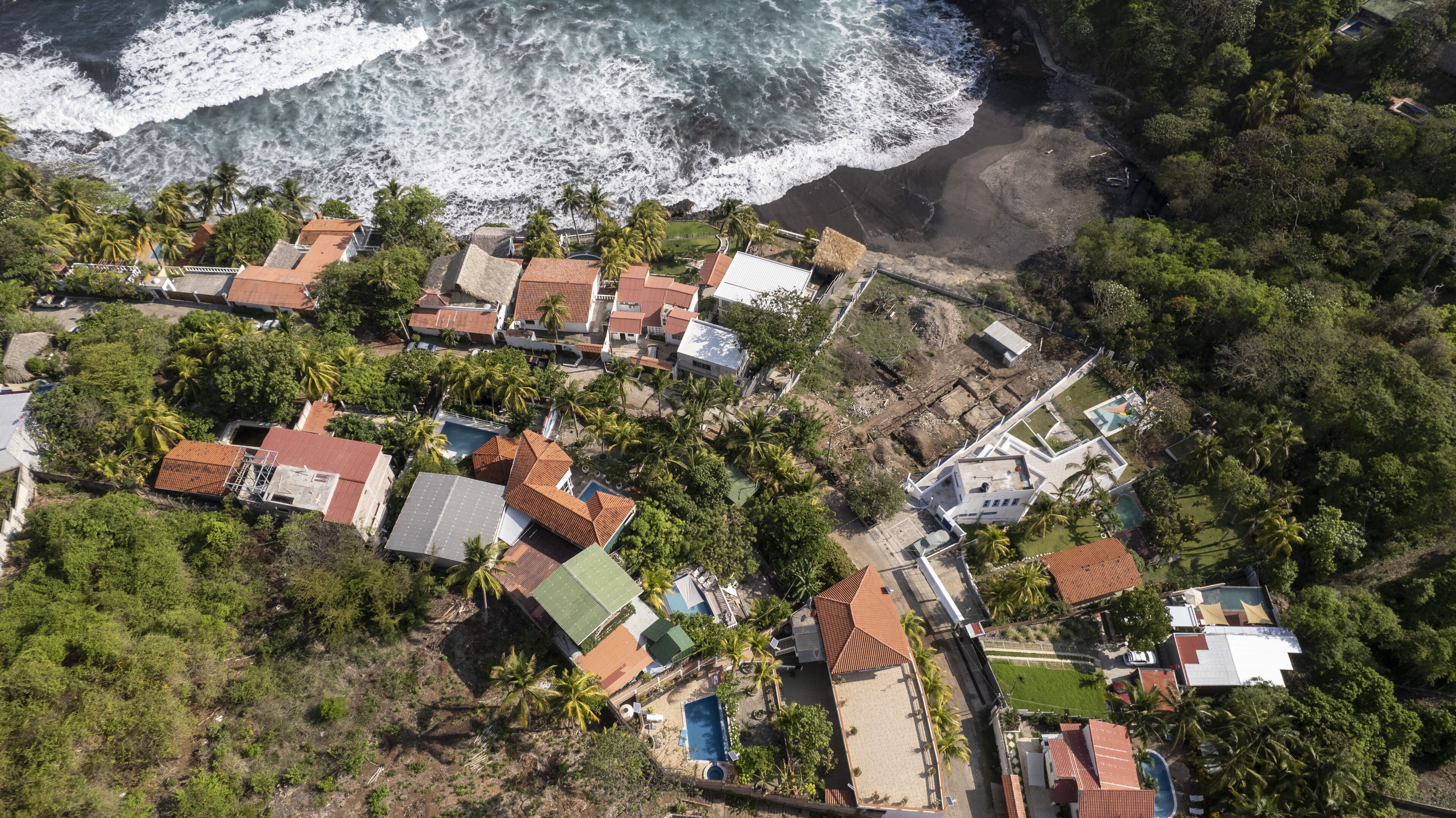 An aerial view of a coastal residential area with houses, a beach, and a large body of water.