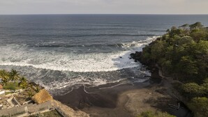 A coastal view with a beach, waves, and a cliff with vegetation. - Beach house El Salvador Brisas Del Mar 99. Just steps from the beach. (Tamanique)