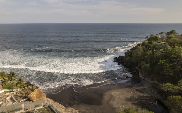 A coastal view with a beach, waves, and a cliff with vegetation.
