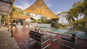 A wooden deck with outdoor seating, a pool, and a view of palm trees and a building. - Beach house El Salvador Brisas Del Mar 99. Just steps from the beach. (Tamanique)