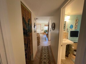 Un pasillo con un tapete estampado, una puerta con un panel decorativo y una vista parcial de un baño con lavamanos y toallero.