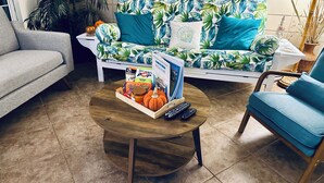 A living room with a grey sofa, a blue armchair, a coffee table with snacks, a remote control, and a plant.