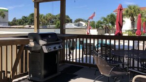 An outdoor patio with a grill, poolside chairs, and umbrellas.