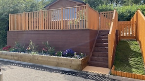 Eine Holzterrasse mit einem kleinen Gebäude, einer Holztreppe und einem Gartenbereich mit Blumen und Pflanzen.