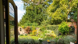 An outdoor patio with a round table and chairs, surrounded by lush greenery and a brick wall. - Miller Cottage - A gorgeous historic cottage in picturesque Saffron Walden (Saffron Walden)