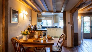 A wooden dining table with chairs, a vase of flowers, and a breakfast setting. - Miller Cottage - A gorgeous historic cottage in picturesque Saffron Walden (Saffron Walden)