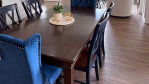 Un comedor con mesa de madera, sillas tapizadas en azul, una planta en maceta y vista al salón.