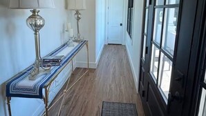 Un pasillo con una consola, dos lámparas, una puerta y ventanas amplias.