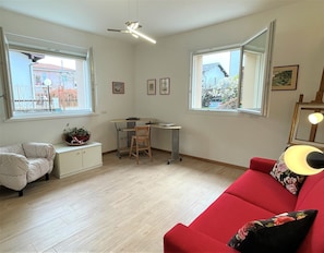 A living room with a red sofa, a white polka dot sofa, a small table with a chair, a desk with a chair, and a ceiling fan.