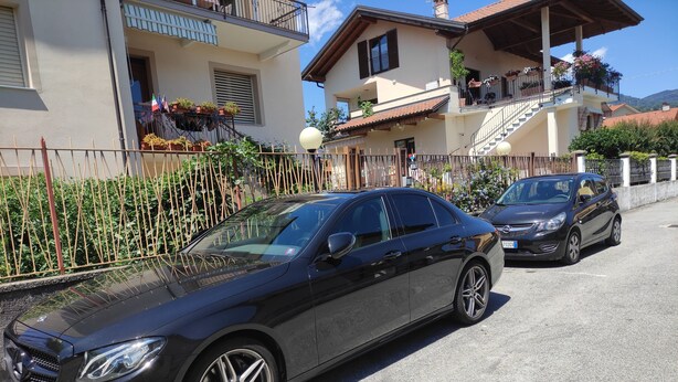 A black sedan parked in front of a building with a balcony and potted plants. - HAPPY DAYS large ground floor apartment with garden and parking. (Intra)