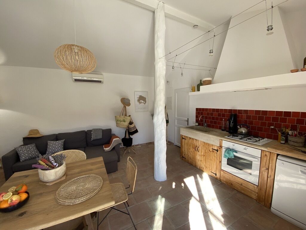 A modern kitchen with a wooden countertop, white cabinets, and a red backsplash. There is a dining area with a wooden table and chairs, and a black sofa with patterned cushions.