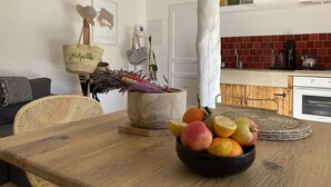 A kitchen with a wooden table, a bowl of fruit, wicker chairs, and a hanging basket. - Mazet des Bambous swimming pool Saint Rémy de Provence (Saint-Rémy-de-Provence)