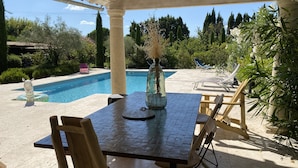 A covered outdoor area with a pool, wooden chairs, and a table with a vase. - Mazet des Bambous swimming pool Saint Rémy de Provence (Saint-Rémy-de-Provence)