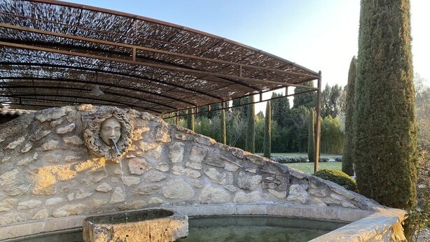 A stone fountain with a statue, surrounded by a stone wall and a pergola structure. - Mazet des Bambous swimming pool Saint Rémy de Provence (Saint-Rémy-de-Provence)