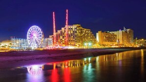 Un hôtel situé au bord de l’eau, avec une grande roue, des bâtiments illuminés et des reflets sur l’eau.