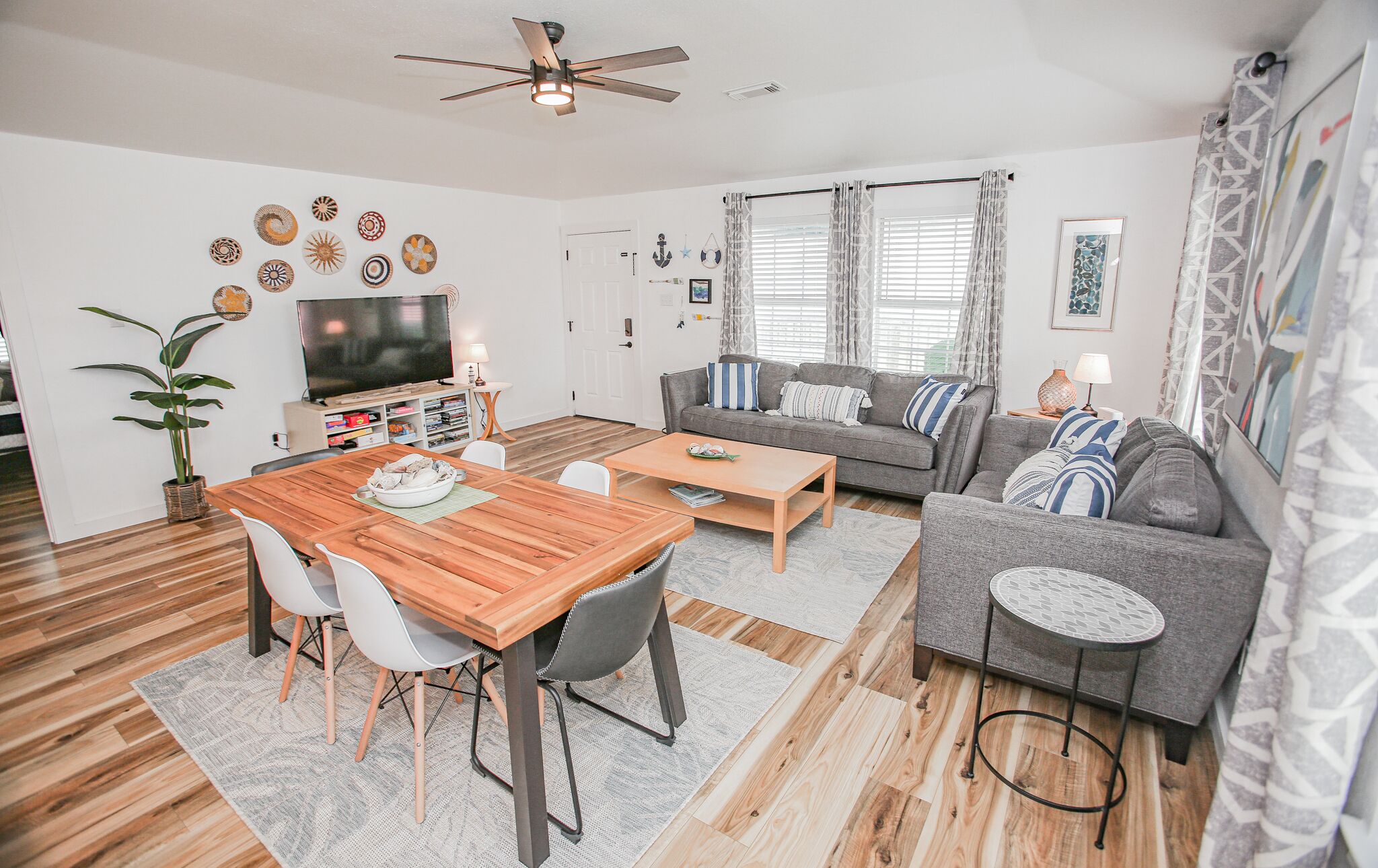 A modern living room with a wooden dining table, grey sofa, and a ceiling fan.