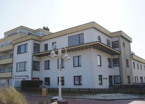 A multi-story residential building with a flat roof, multiple windows, and a visible balcony on the upper floors. - Strand-zeit - ein Steinwurf zum Meer (Wangerooge)