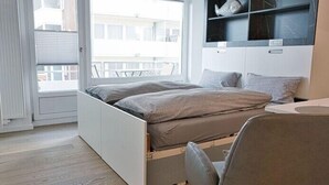 Een moderne slaapkamer met een bed, een bureau en een raam met uitzicht op een balkon.