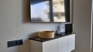 Een moderne woonkamer met een flatscreen televisie aan de muur, een houten schaal op een witte kast en een witte radiator.