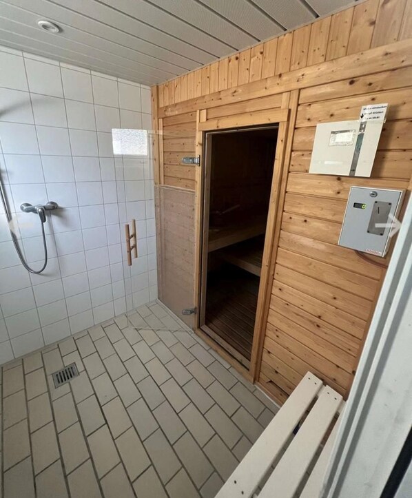 A bathroom with a shower, wooden walls, a tiled floor, and a wooden door. - Strand-zeit - ein Steinwurf zum Meer (Wangerooge)