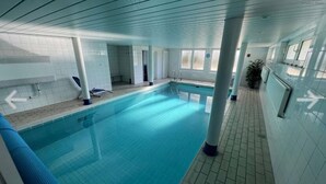 Een binnenzwembad met helderblauw water, betegelde wanden en een betegelde vloer.