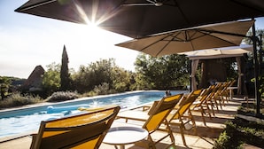 A poolside area with lounge chairs and umbrellas, overlooking a swimming pool and natural landscape.