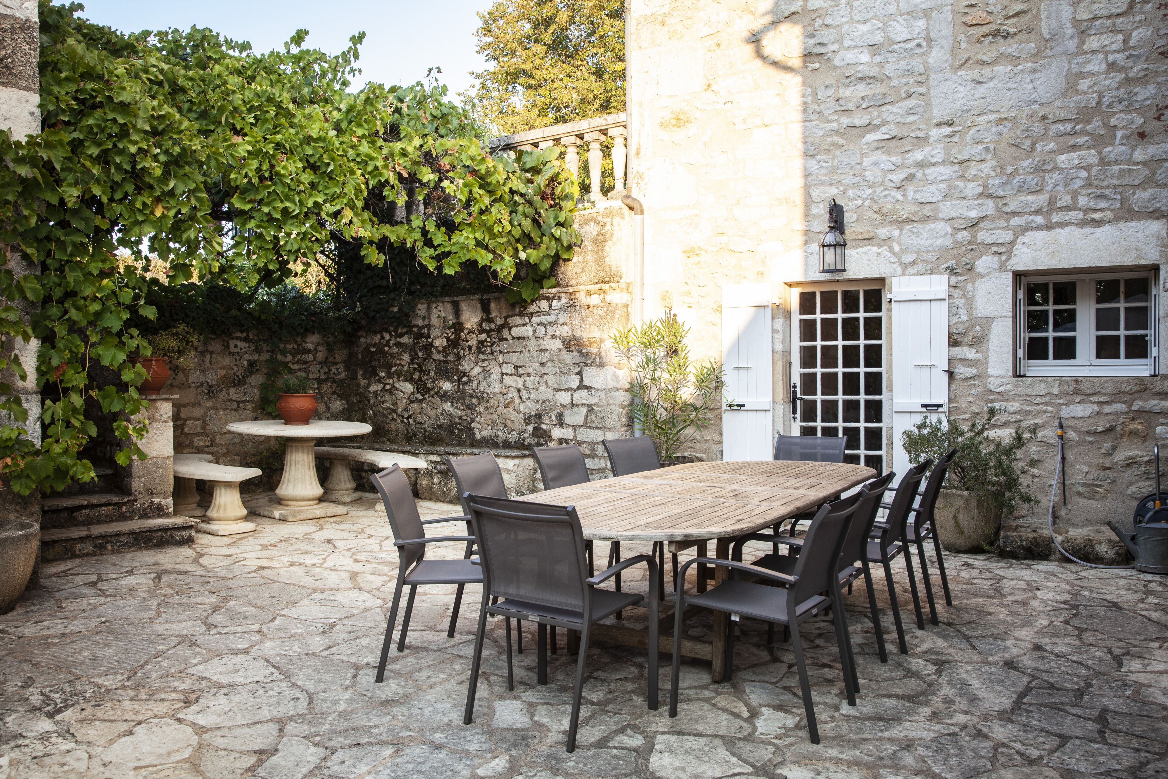 An outdoor patio with a stone floor, a wooden table, and metal chairs.