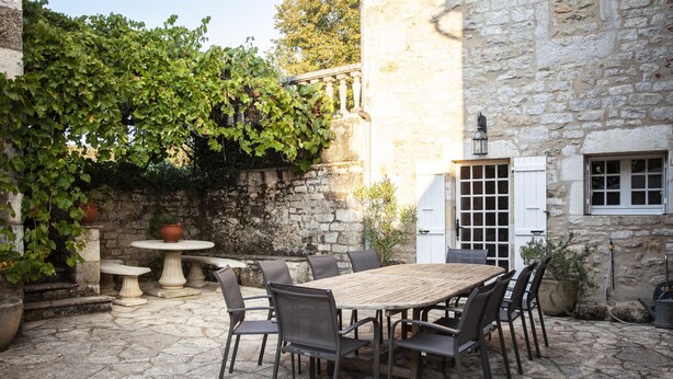 Une terrasse extérieure avec un sol en pierre, une table en bois et des chaises en métal.
