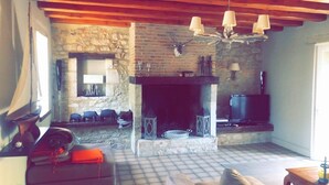 A rustic living room with a stone fireplace, wooden beams, a television, and a cozy seating area.