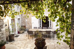 An outdoor patio with a stone floor, a wooden table, and chairs. There are potted plants and a stone wall in the background. - IN BALANCE. A COUNTRY HOUSE FULL OF CHARACTER (Carnac-Rouffiac)