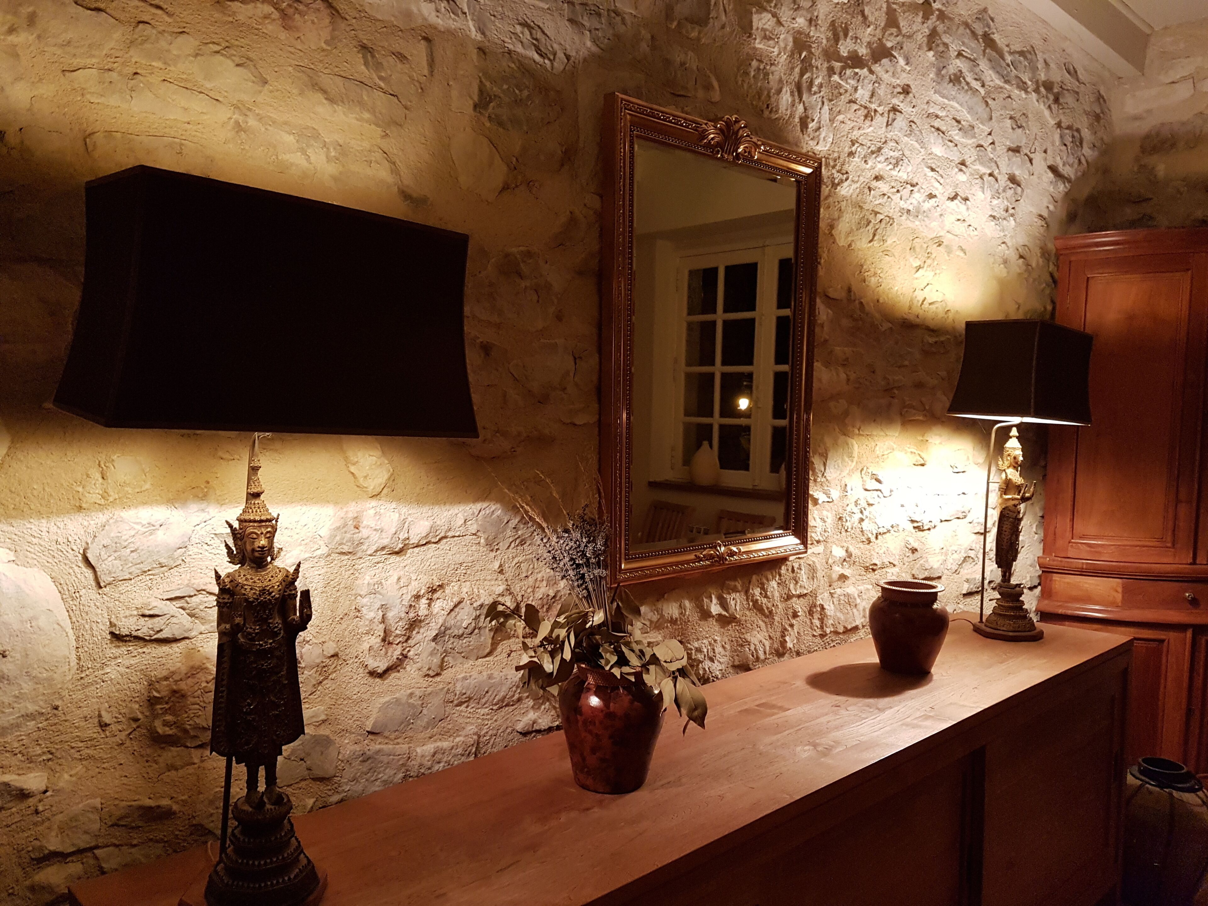 Une salle de bain rustique avec un mur en pierre, un meuble-lavabo en bois, un miroir et une statue.