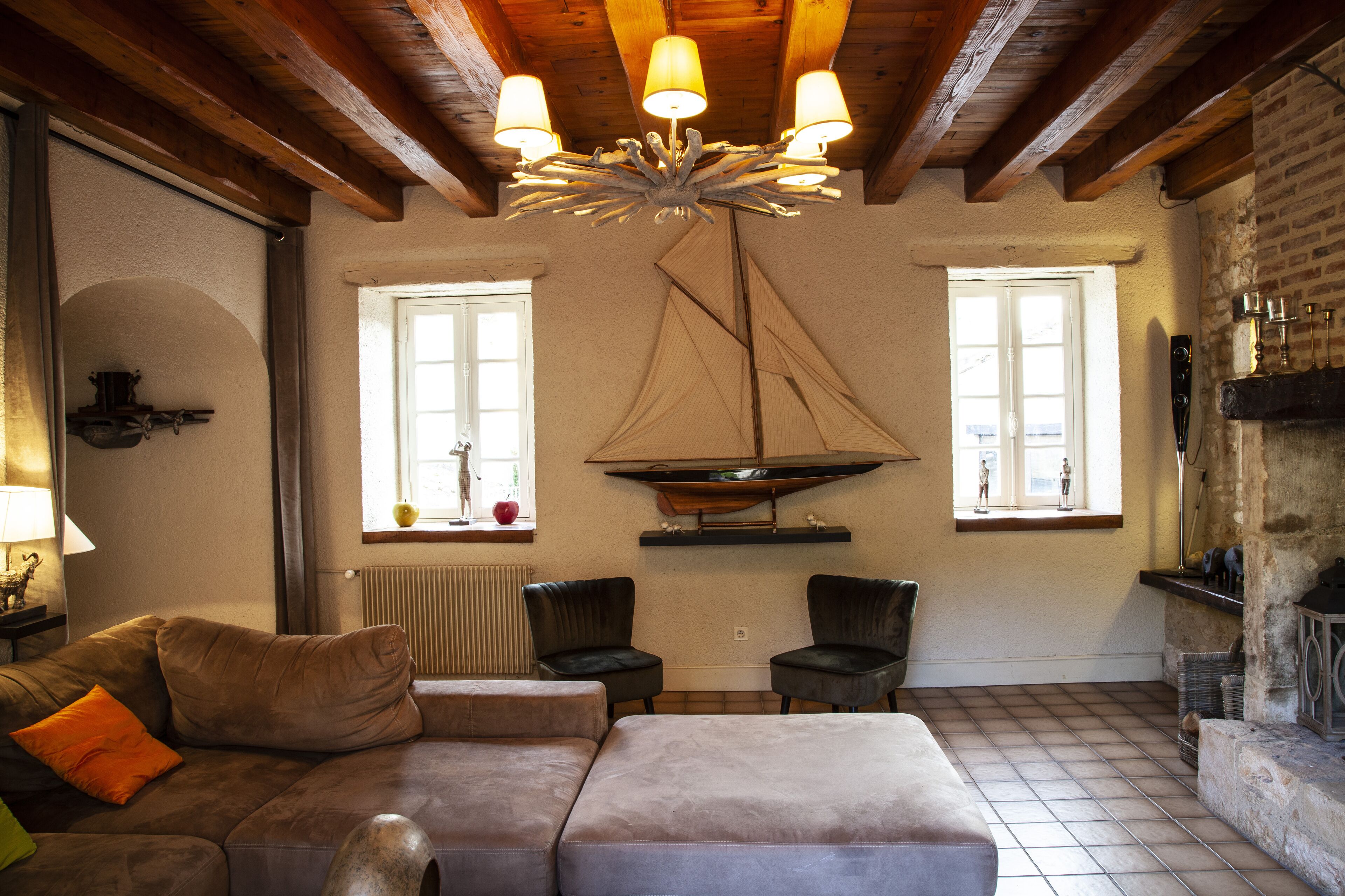 Una sala de estar acogedora con un sofá de cuero marrón, dos sillones negros, techo de madera y una chimenea.