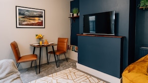 Un salon moderne avec un téléviseur à écran plat fixé sur un mur bleu foncé, un coin repas comprenant deux chaises et une petite table, et un canapé.