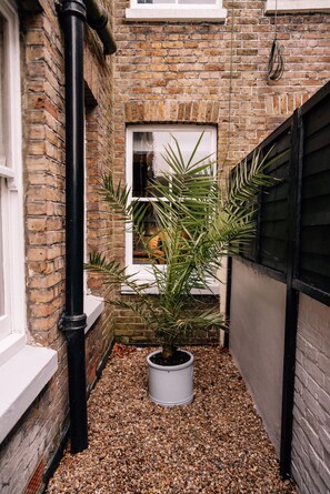 A narrow alleyway with a potted plant, a window, and a brick wall. - Sanctuary-by-Sea  2 bed Apartment (Worthing)
