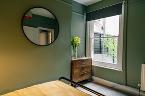 A bedroom with a bed, a dresser, a mirror, and a window with a view of greenery outside.