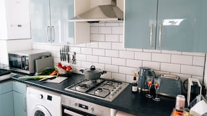 Une cuisine moderne équipée d’une cuisinière à gaz, d’un four à micro-ondes et d’un four encastré. On y trouve des placards, un évier et divers ustensiles de cuisine.