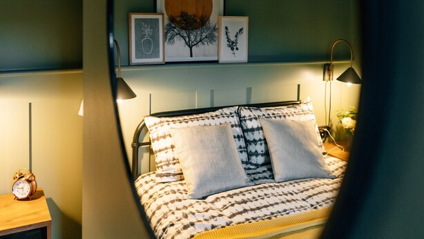 Une chambre à coucher comprenant un lit, une table de chevet, une lampe et des œuvres d’art accrochées au mur.