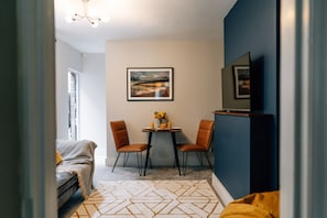 Um espaço compacto com área de refeições, um sofá, uma TV fixada na parede e um quadro emoldurado sobre a mesa.