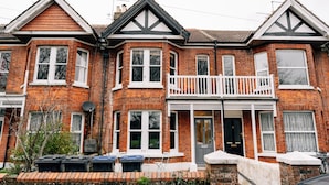 Une maison à deux étages, construite en briques, avec un balcon, une porte d’entrée et une antenne parabolique.