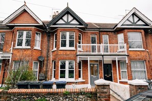 A two-story brick house with a balcony, a front door, and a satellite dish. - Sanctuary-by-Sea  2 bed Apartment (Worthing)