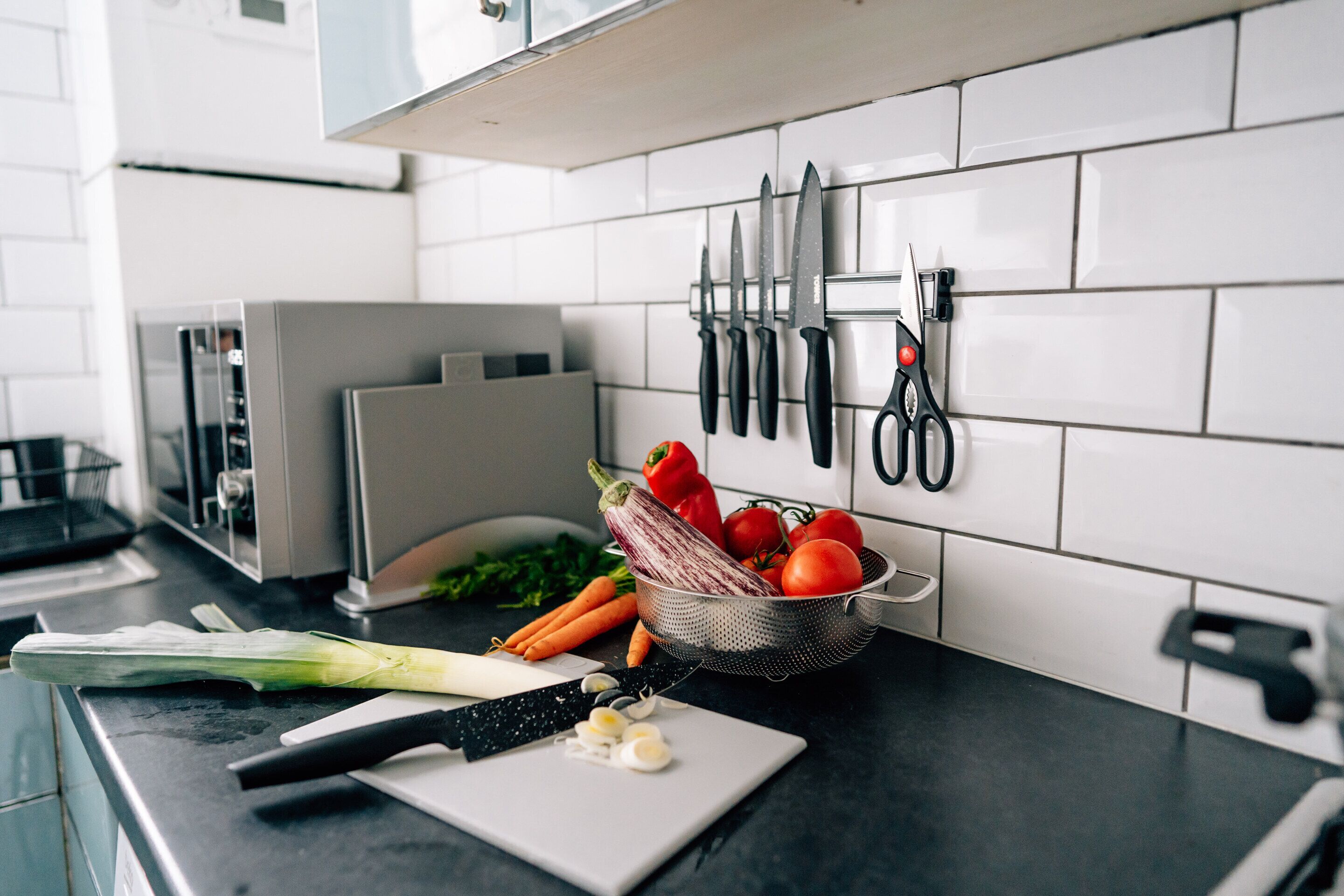 Un plan de travail de cuisine avec une planche à découper, des légumes et une passoire.