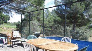 An outdoor seating area with a wooden table and chairs, a wicker chair, and a view of a swimming pool surrounded by trees. - Country house in the heart of nature (mouriès)