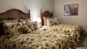 Een slaapkamer met twee houten bedden, bloemenbeddengoed, een plafondventilator en een lijst met een afbeelding aan de muur.
