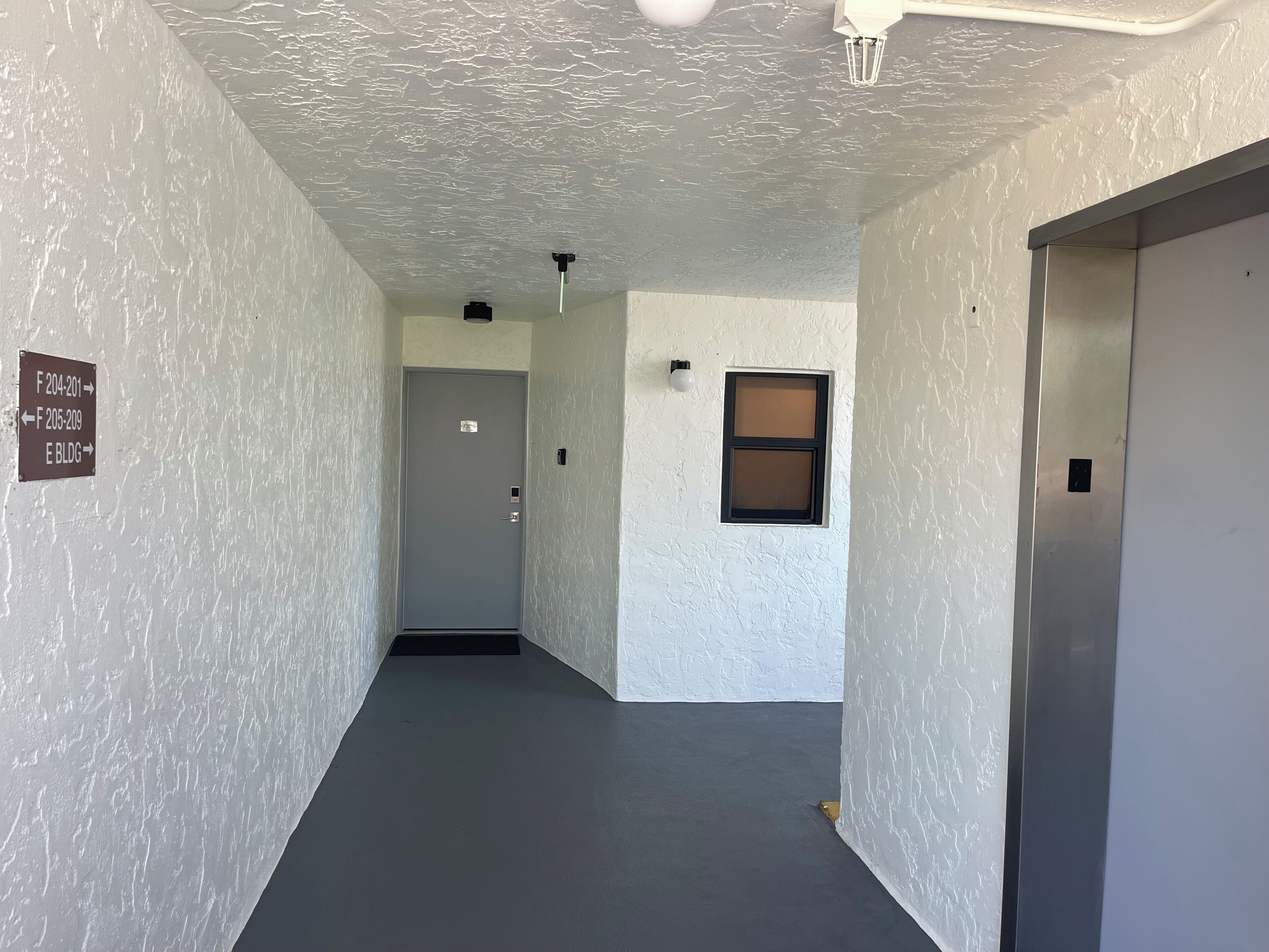A hallway with a textured white wall, a door at the end, and a small window with a black frame.
