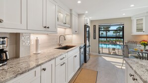 Una cucina moderna con mobili bianchi, piani di lavoro in granito e forno integrato. Si apre su un balcone con vista sulla piscina.