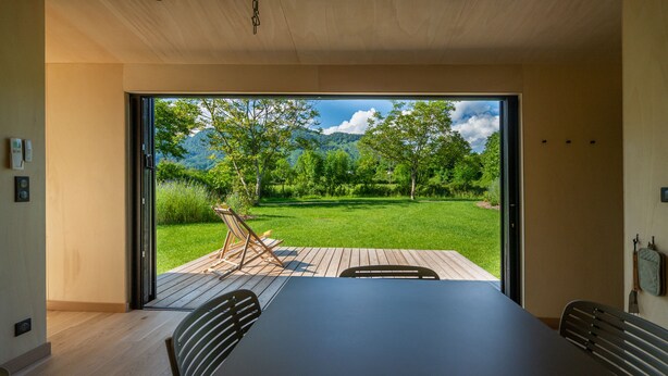 A modern room with a large sliding glass door leading to a deck with a view of a lush garden and mountains. - ICI - Tiny house 40 m2 for 4 people (Arette)