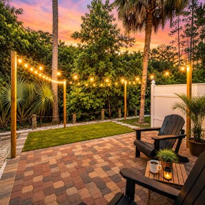 A patio with a brick floor, a wooden bench, a chair, and string lights. - Cape Coral FL (Cape Coral)
