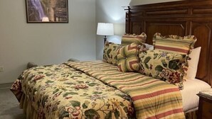 A bedroom with a bed, a nightstand, a lamp, a ceiling fan, and a painting on the wall.