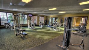 A gym with various exercise equipment, large windows, and a carpeted floor.