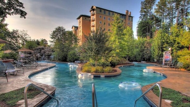 A hotel pool area with a hot tub, lounge chairs, and a building in the background.